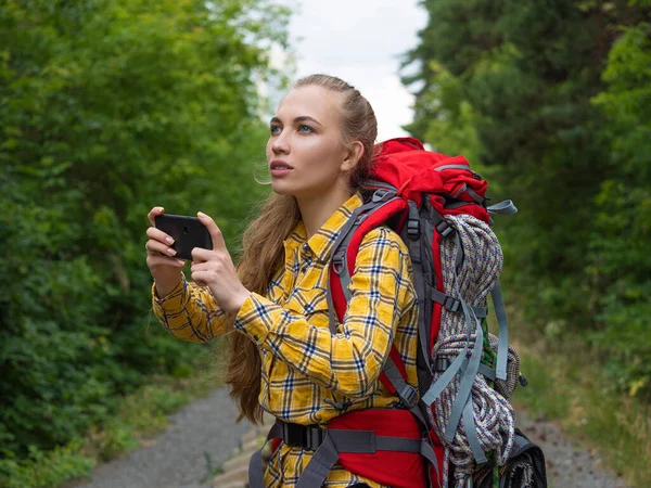 Caminhante feminina olhando para seu telefone celular segurando-o com as duas mãos . — Fotografia de Stock