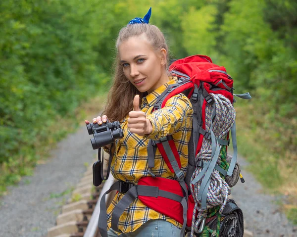 Mulher caminhante com binokular olhando para a câmera e mantendo o polegar para cima . — Fotografia de Stock