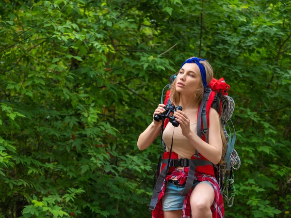 Hiker woman with a backpack walks through the forest with binoculars. — Stock Photo, Image