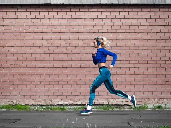 Mujer corriendo al aire libre en un día soleado. Fondo de pared de ladrillo. — Foto de Stock