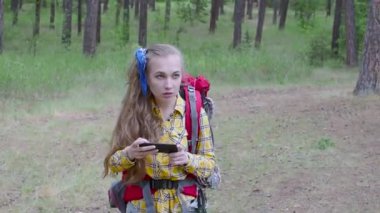 Sırt çantalı bir kadın ormanda yürüyor ve cep telefonuyla fotoğraf çekiyor..
