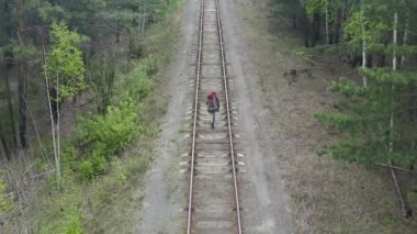 Sırt çantalı bir kadın, tren yolu boyunca ormanda yürüyor. Hava manzaralı..