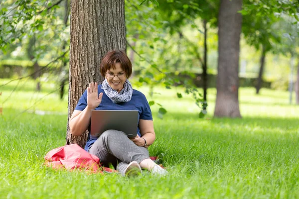 Happy middle-aged woman enjoying online talking with her friends and kids. She saying hello with a palm of hand