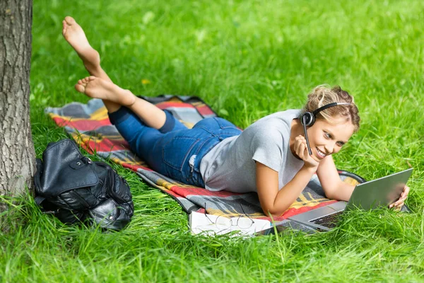 Młoda kobieta - ogląda webinarium edukacyjne na laptopie, siedzi na zielonej trawie. Koncepcja kształcenia na odległość. — Zdjęcie stockowe