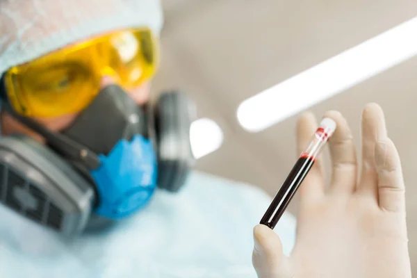 Forskare i skyddsdräkt tittar noga på ett blodprov i ett provrör. Närbild. — Stockfoto