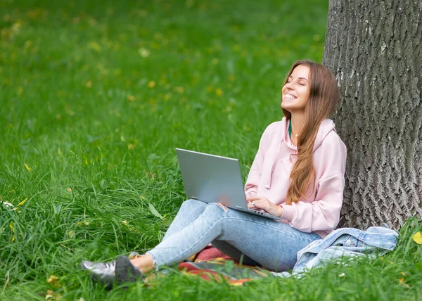 Smiling young woman with laptop in public park. Stock Photo