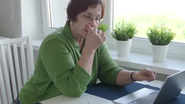 Przemyślana starsza kobieta pracująca w domu za pomocą laptopa. Odwraca wzrok. — Wideo stockowe