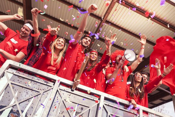 группа болельщиков, одетых в красное, смотрящих спортивное событие на трибунах стадиона
