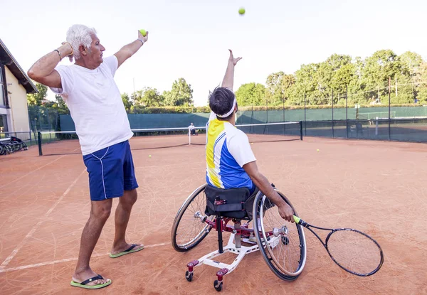 tennis coach teaching a disabled player the correct movement of the service