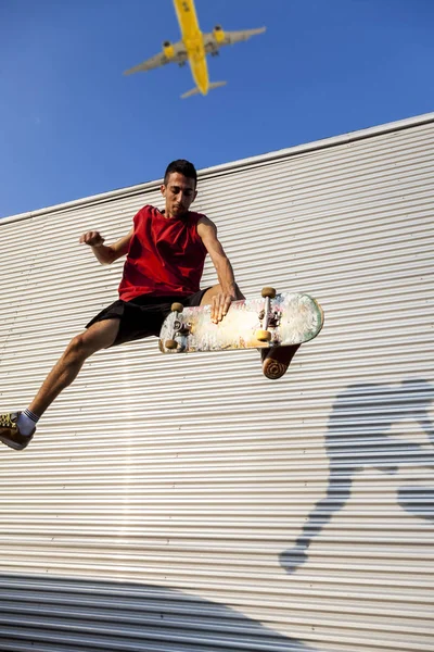 若いスケートボーダーが放棄された建物の屋根の上に金属の背景の前に彼のボードに飛び上がる — ストック写真
