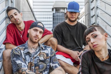 group of young rappers posing sitting on the metal stairs of an abandoned building clipart