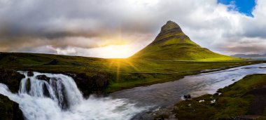panoramik Kirkjufell dağ ve bulutlu gün batımında şelale