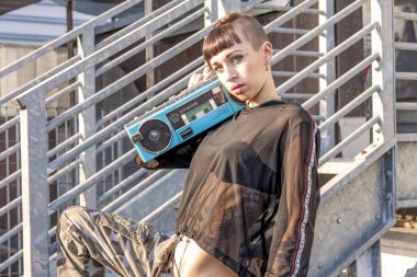 Genç kadın şarkıcı rap beyaz dövmeli bir stereo radyo metal merdiven ile poz
