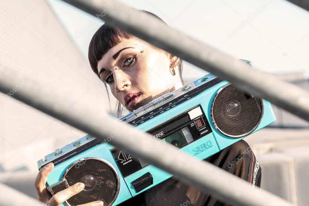 young female singer rap caucasian tattooed posing with a stereo radio on a metallic ladder