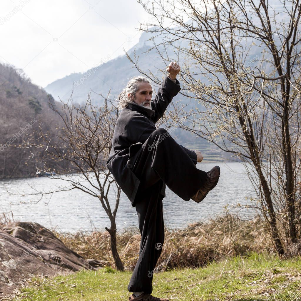 mature man practicing Tai Chi discipline outdoors in a lake park on a winter day