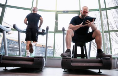 spor salonunda sürüş makineleri üzerinde tablet bakarak rahatlatıcı iken koşucu atlet