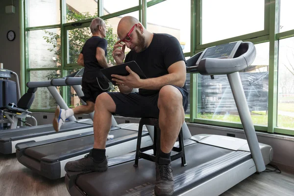 runner athlete while relaxing looking at the tablet on the driving machinery in the gym