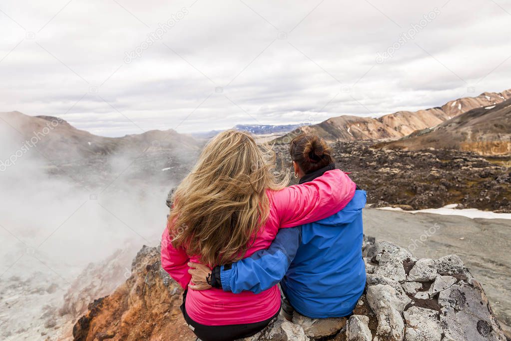 two female traveling friends hugging each other watching the landscape from the top of a volcano in Iceland