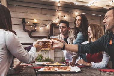 Mutlu arkadaş grubu bira içip pizza yiyor.