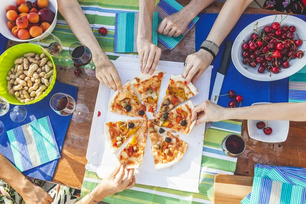 Handen van vriendinnen delen pizza van een tafel — Stockfoto