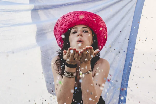 Bonita mujer con colorido sombrero de paja soplando confeti —  Fotos de Stock