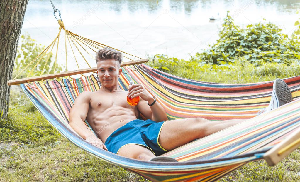 young muscular adult drinking a red drink lying in a hammock