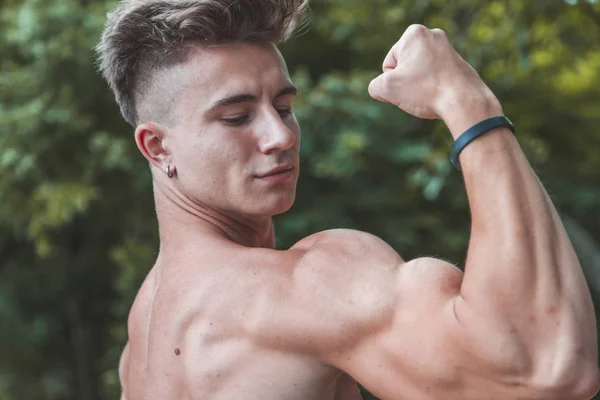 Jovem adulto muscular mostrando seu bíceps ao ar livre — Fotografia de Stock