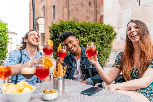 Friends drinking colored cocktail at outdoor bar - New normal lifestyles concept with happy people toasting drinks outside