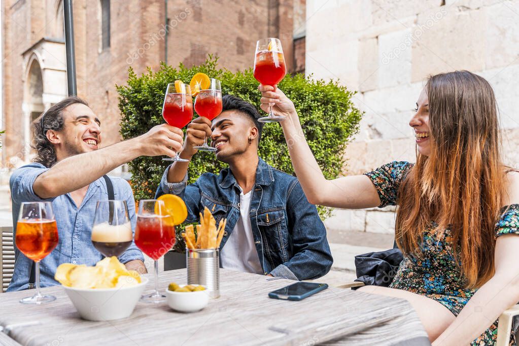 Friends drinking colored cocktail at outdoor bar - New normal lifestyles concept with happy people toasting drinks outside