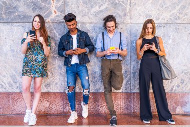 Sosyal ağlardaki içeriği paylaşmak için akıllı telefonları kullanan bir grup çok ırklı arkadaş duvarın önünde.