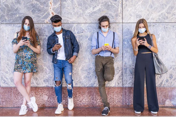 Yüz maskeli çok ırklı arkadaşlar sosyal ağlardaki içeriği paylaşmak için akıllı telefon kullanıyorlar.