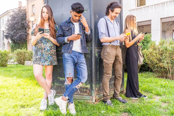 Sosyal ağlardaki içeriği paylaşmak için akıllı telefonları kullanan bir grup çok ırklı arkadaş duvarın önünde.