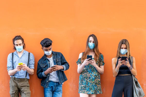 group of multiracial friends with face masks in front of orange wall using smartphones to sharing content on social networks