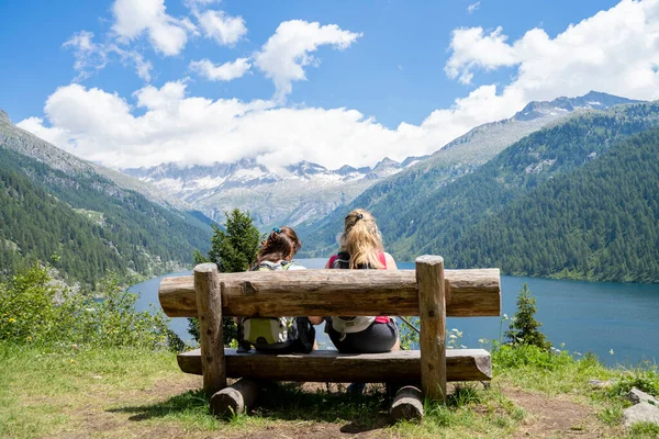 Två Kvinnliga Vänner Avkopplande Sitter Träbänk Framför Fjällsjö — Stockfoto