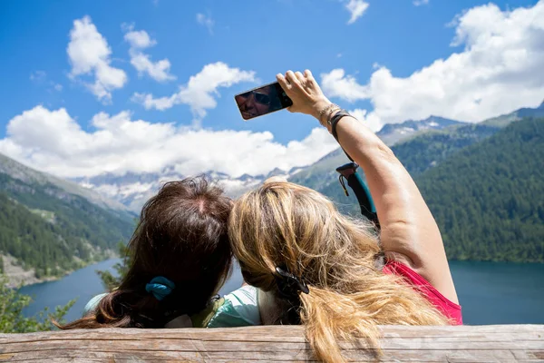 Due Amiche Fanno Selfie Sedute Una Panchina Legno Fronte Lago — Foto Stock