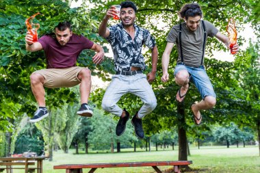 Bir grup milenyum insanı dışarıda renkli kokteyller içerken zıplayarak eğleniyor.