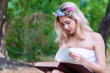 Elinde kitap okurken, parkta düşen sonbahar yapraklarının üzerinde oturan sevimli genç bir kadın. Çiçekli neşeli sarışın kız kitaptan öğreniyor. Ağacın altında rahatlıyor..