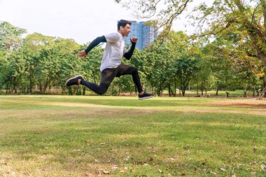 Enerji egzersizi eğitimi almış yakışıklı genç bir atlet ve halka açık parkta büyük yeşil bir ağaçla dışarı atlıyor. Aktif sağlık ve motivasyon yaşam tarzı ve hırs kavramı
