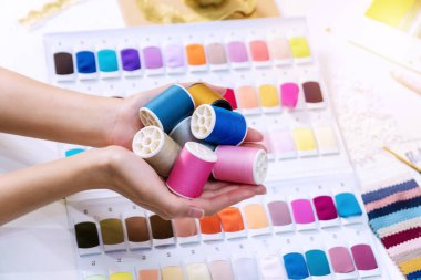 Terzi kadının ellerini kapatın. Masanın üzerinde bir sürü farklı parlak renk ipliği var. Terzi kız dikiş işi yapıyor ve elinde bir sürü iplik makarası tutuyor ve yeni ürünlerle ilgili rüyalar görüyor..