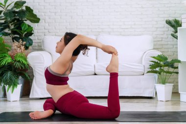 Oturma odasında yoga eka pada rajakapotasana yaparken beyaz kanepenin önünde oturan hareketli genç kadınlar. Rahatlayan kız evde yoga yapıyor. Yaşam tarzı sağlıklı konsept.