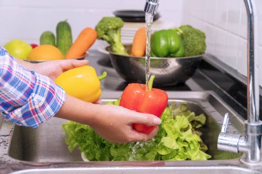 Woman hand washing vegetables using water supply at sink in kitchen for cooking some fresh salad for good health. Hand girl cleaning red sweet pepper with water to flush out toxins. clipart