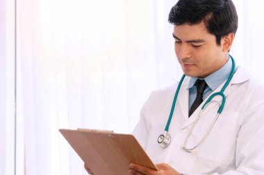 Tıp doktoru ofisinde otururken raporunu okuyor. Yakışıklı genç adam rapor kağıdına bakarken elinde belge olan üniformalı bir doktor tutuyor..