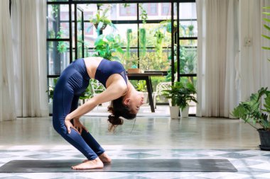 Aktif genç kadınlar mavi spor giyerler ve paspasın üzerinde yoga sekansı yaparlar. Rahatlayan kız yoga pratiği yapıyor. Vücudunu evde formda tutuyor. Sağlıklı konsept için yaşam tarzı egzersizi.