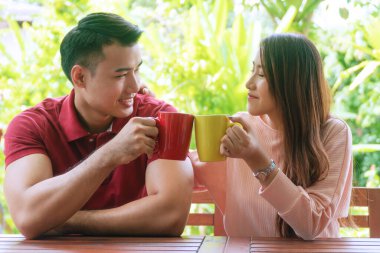Evdeki bahçede sandalyede otururken ellerinde kahve ya da çay tutan neşeli genç bir çift. Romantik aşıklar sabahları bardakta sıcak kahve içerler..