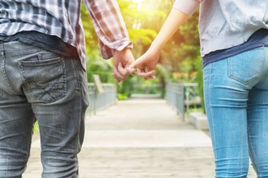 Genç çiftin elleri ahşap köprü altyapısı ile parmaklarını çapraz tutan kot pantolon giyer. Romantik yakışıklı genç adam parkta dururken kız arkadaşının elini tutuyor. ilişki kavramı.