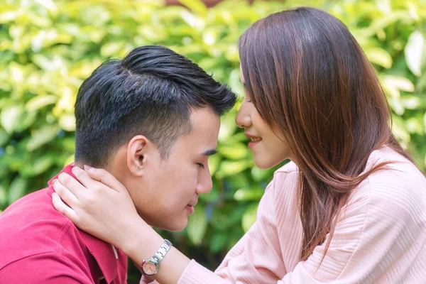 Charming young woman kiss forehead her boyfriend with love while sitting in the garden. Sweet romantic young couple embracing together at home. Relationship lover concept.