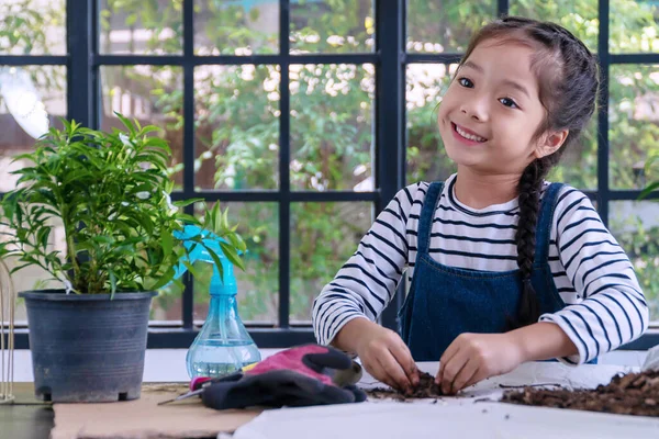陽気な小さな女の子は 温室で鍋に小さな花を計画しながら ツールと混合した黒い土を再生します ライフスタイルコンセプト — ストック写真