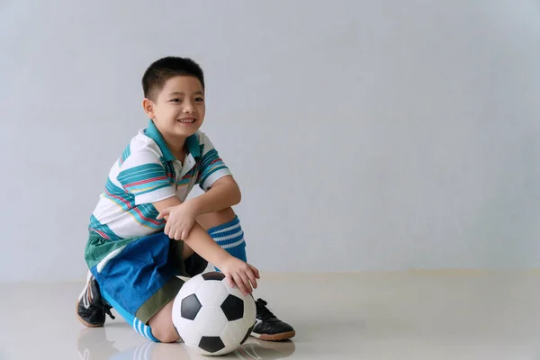 カメラを見ながら床に座ってサッカーと陽気なかわいい男の子 女子高生は部屋に座っている間 ボールの笑顔でサッカーのスポーツウェアを着ています ライフスタイルキッズウェルネスコンセプト — ストック写真