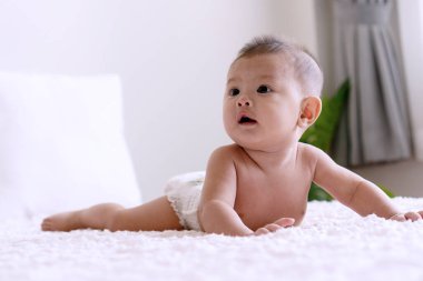 Neşeli şirin bebek beyaz yatakta uzanıyor ve bir şeye ya da aileye bakıyor. Yeni doğan çocuk evdeki yatakta oynarken bebek bezi takıyor..