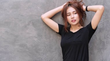 Büyüleyici genç bayan, gri duvar arkasında kalın saçlarını tutarak rahatlıyor. Uzun kahverengi dalgalı saçlarını at kuyruğuyla bağlayan neşeli kız fotokopi alanı olan bir şeye bakıyor..